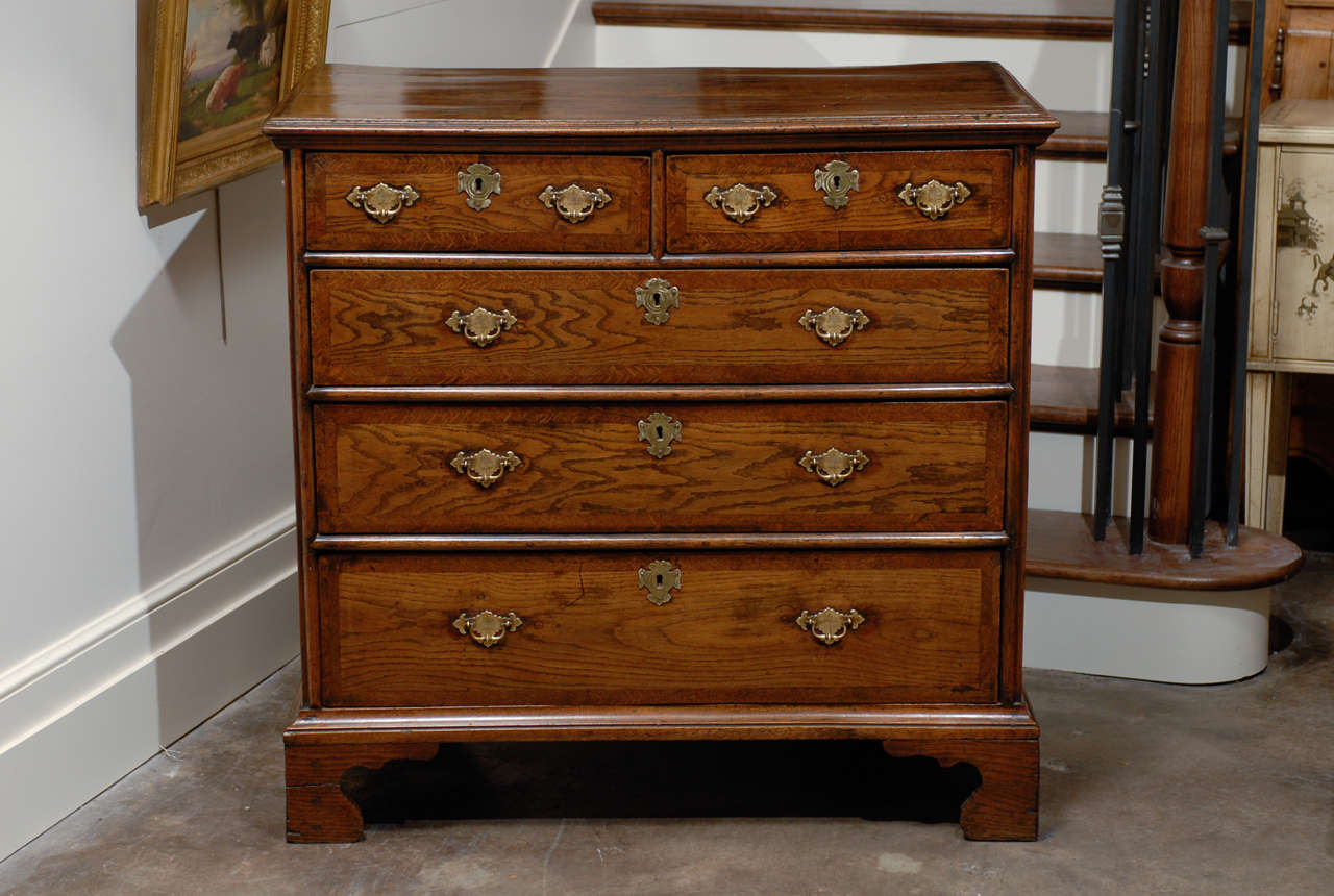 An English Regency period five-drawer commode with banding on the drawers and ogee bracket feet from the early 19th century. This English chest, circa 1820 features a rectangular top with beveled edge over two smaller drawers surmounting three