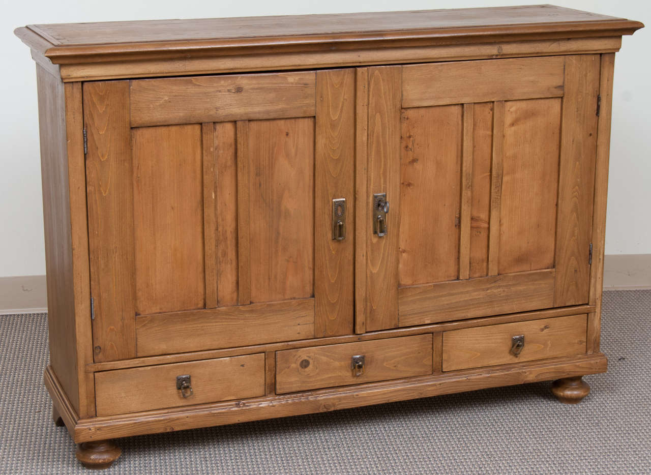 A most useful low and shallow pine base featuring two panelled doors above three hand-cut dovetailed drawers.  Perfect as a TV stand or hall cupboard.  All original hardware to doors and drawers