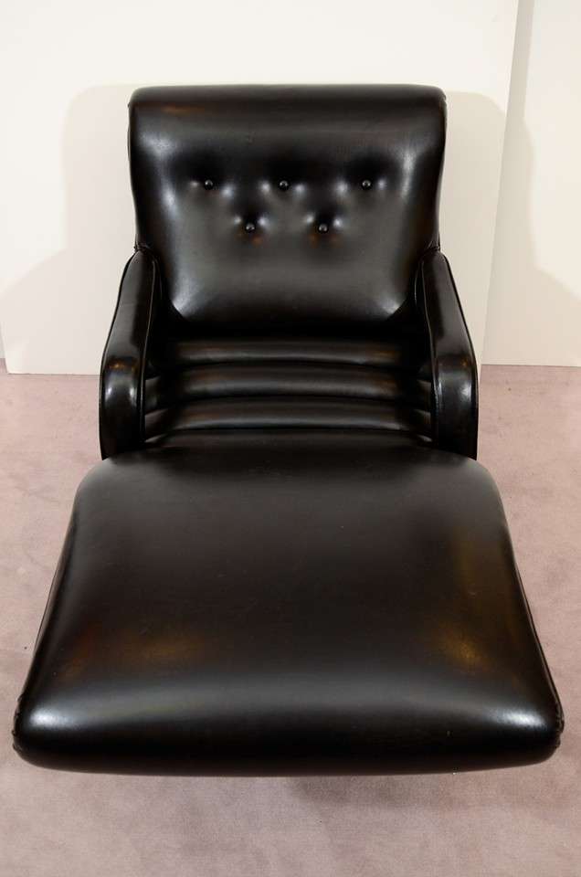 A vintage reclining lounge chair in black leather with button tufted seat back and brass nail head detailing.