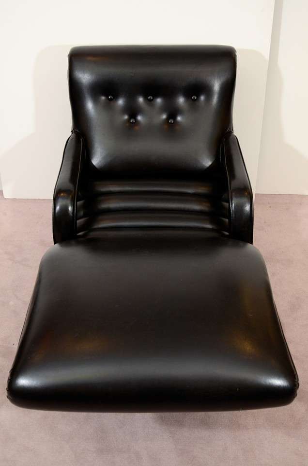 A vintage reclining lounge chair in black leather with button tufted seat back and brass nail head detailing.