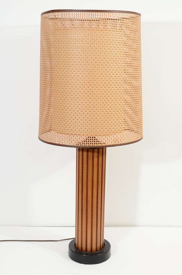 A pair of vintage table lamps, produced circa 1960s, with fluted wood cylindrical stems and drum form shades, each with an outer layer of woven rattan. Good vintage condition, consistent with age and use.