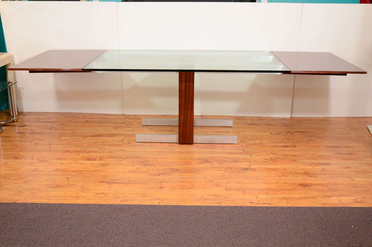 A vintage dining table by noted designer Vladimir Kagan. The piece has a central thick cut glass surface flanked by two removable rosewood leaves and sits on a base of rosewood and aluminum.