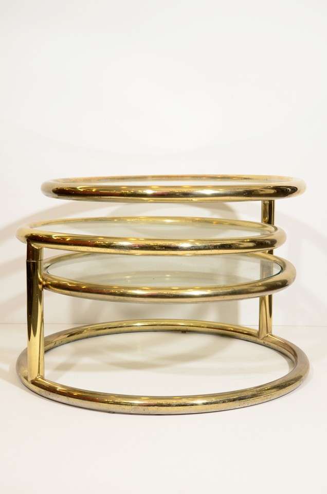 A vintage circular coffee or cocktail table with three pivoting tiers. The piece is in good vintage condition with age appropriate wear; some scratches to glass and brass.