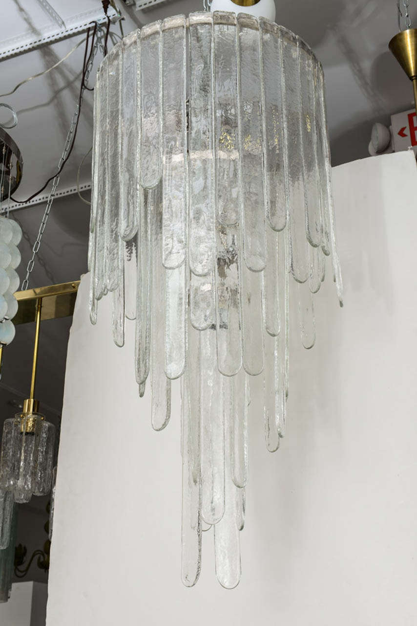 Mazzega chandelier featuring hammered  glass bars that resemble rounded, falling icicles hanging from a circular three tiered chrome structure with 11 light sockets in total.