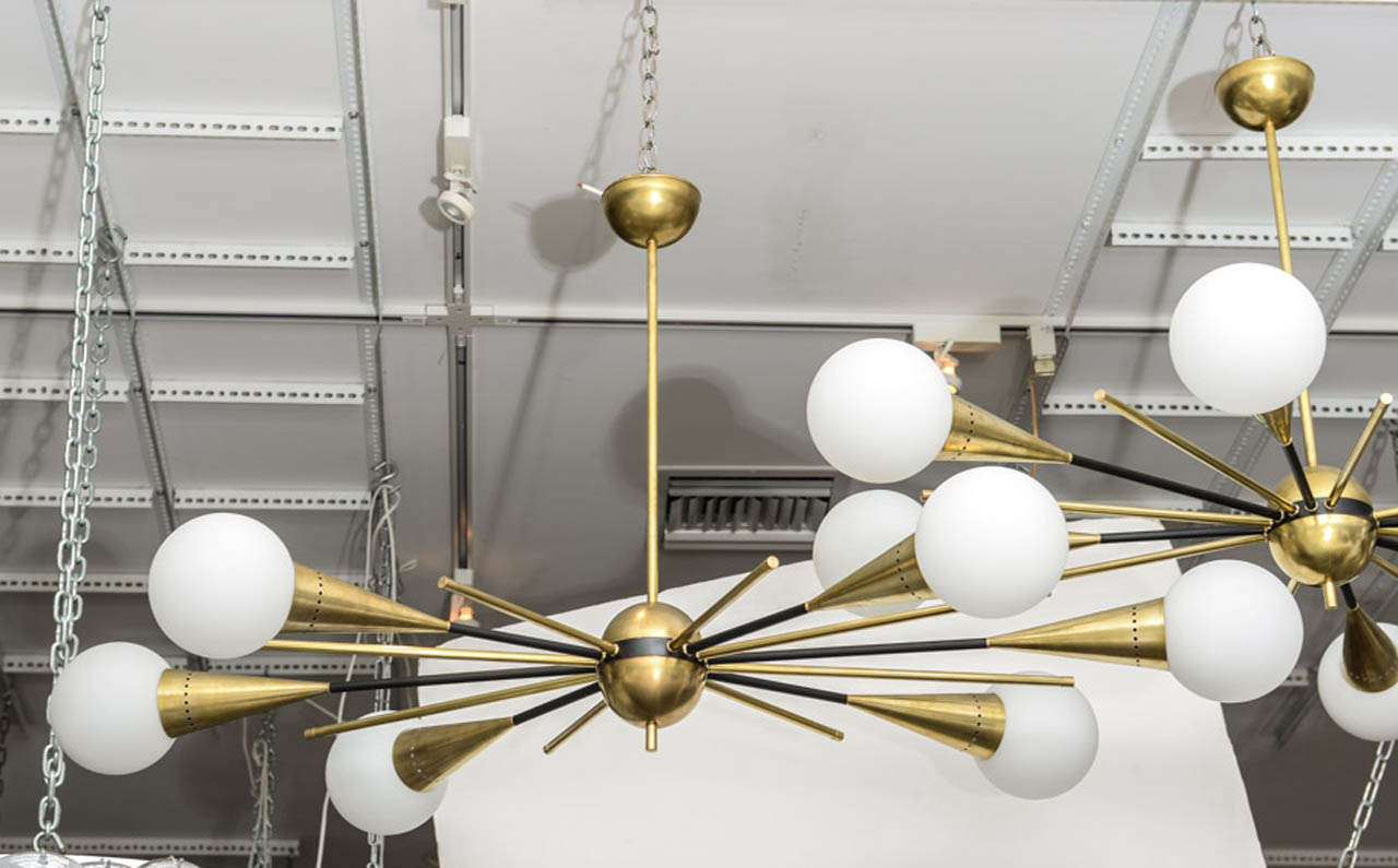 Two massive horizontal line sputnik chandeliers featuring alternating rays of blackened brass and light satin finished brass - with 6 frosted white satin globes.