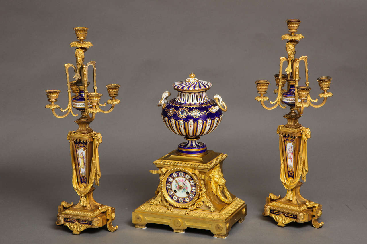 A beautiful antique French royal blue Sèvres Porcelain and French ormolu-mounted three-piece clock garniture set. The clock having bronze lion head handles; the five-light candelabrum with ram's heads and medusa head masks. The porcelain with raised