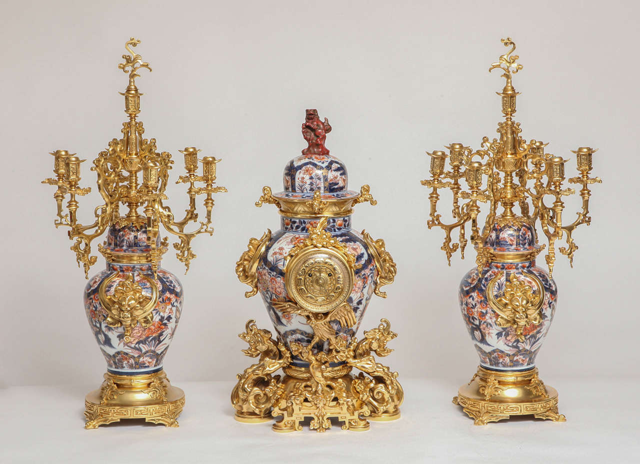 Une très belle pendule française ancienne à trois pièces en porcelaine de Chine, bronze doré et Imari. La porcelaine est merveilleusement peinte à la main avec des fleurs, des pêches, des oiseaux et des nuages aux motifs complexes. Avec une
