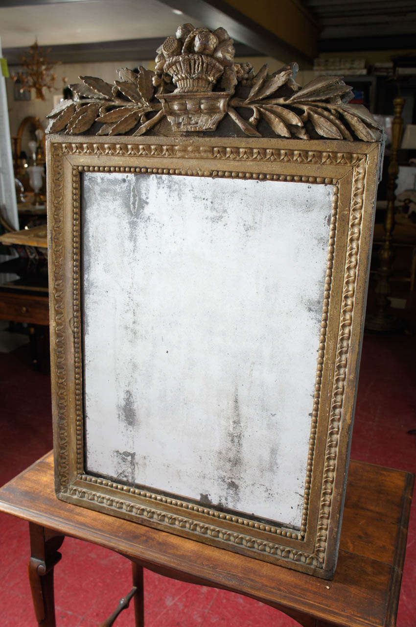 Classical detailing on frame of rows of lambs tongue and beading, giltwood mirror. At the top, the applied decoration is composed of a centered basket of fruit and flowers flanked by bay leaf branches. The mirror is original and the backing is wood.