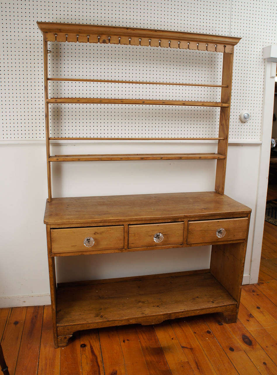 Open-back shelf cupboard with plate rails. This wonderful pine piece has a scalloped frieze, three drawers with original glass pulls, bracket feet and a handy lower shelf.