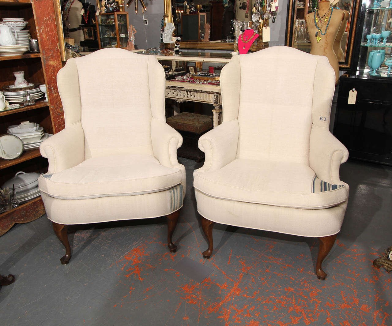 Comfortable pair of wingback chairs reupholstered in linen and ticking with monograms and original repairs. Reversible down filled cushions.