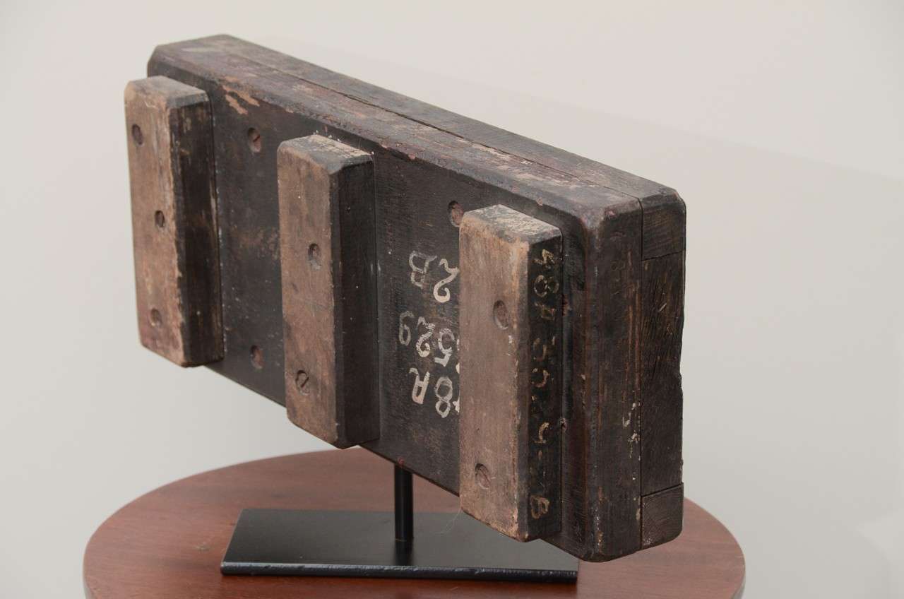 Wooden Mold on black metal stand with engravings and dark red paint residue from use. The back and sides of the mold is marked in white numbers.