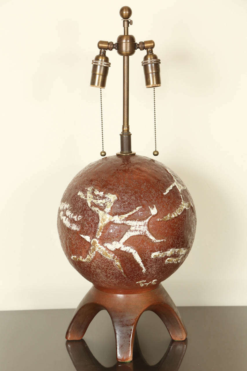 Interesting tripod/ball ceramic lamp.  The base is fired in one piece, with primitive running figures picked out in white glaze.
The lamp has been newly rewired with new double cluster hardware in a bronze finish.