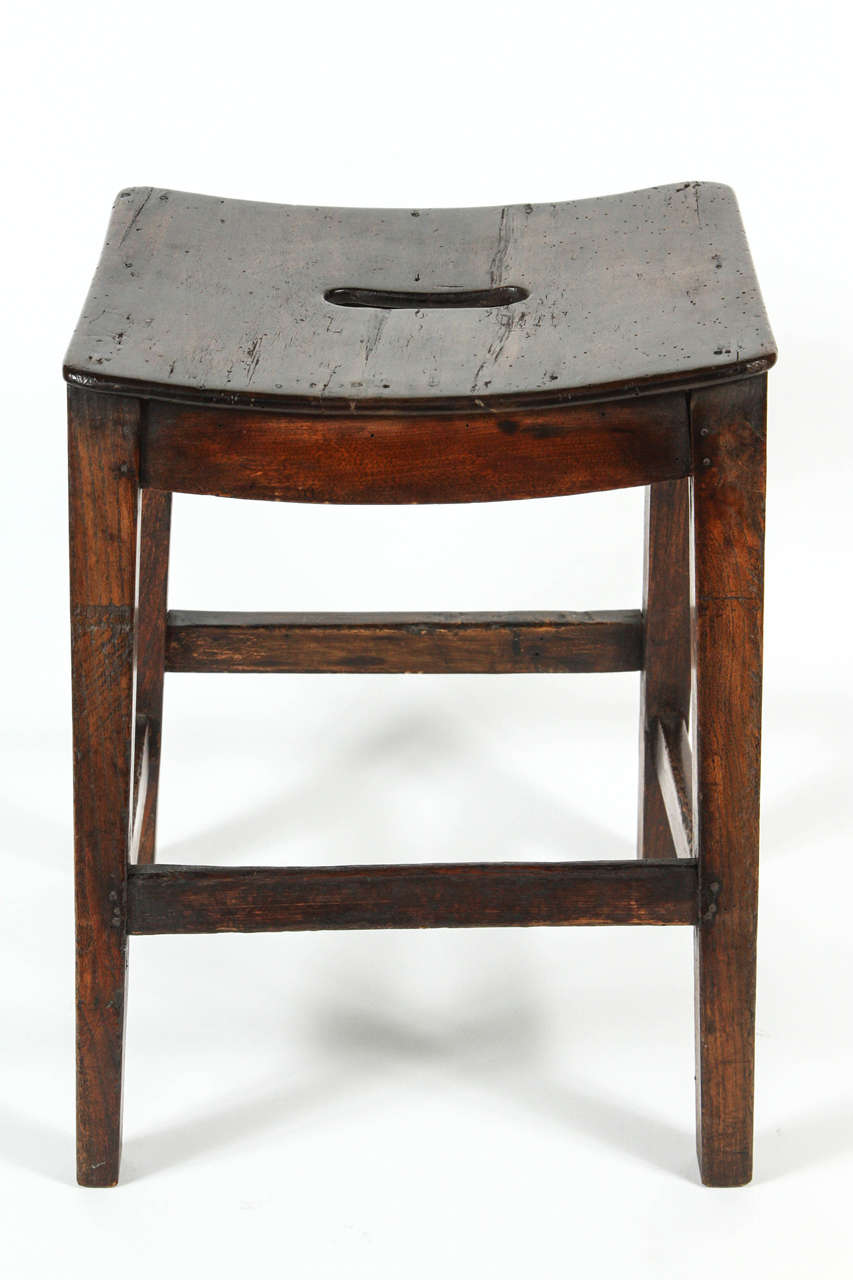 An English Elm Stool with stretchers, hand-hold cutout and saddle seat, 19th century