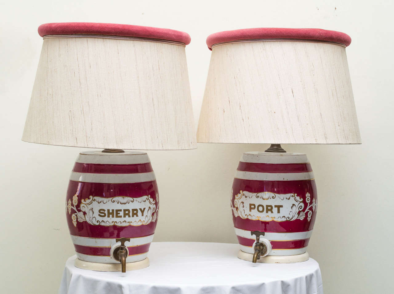 Pair of matched ceramic English port and sherry crocks as custom lamps. Complete with old brass taps. Three way switches with light diffuser shades. Good antique patina. With wood bases and linen shades. Ceramic crocks are 13 inches high.