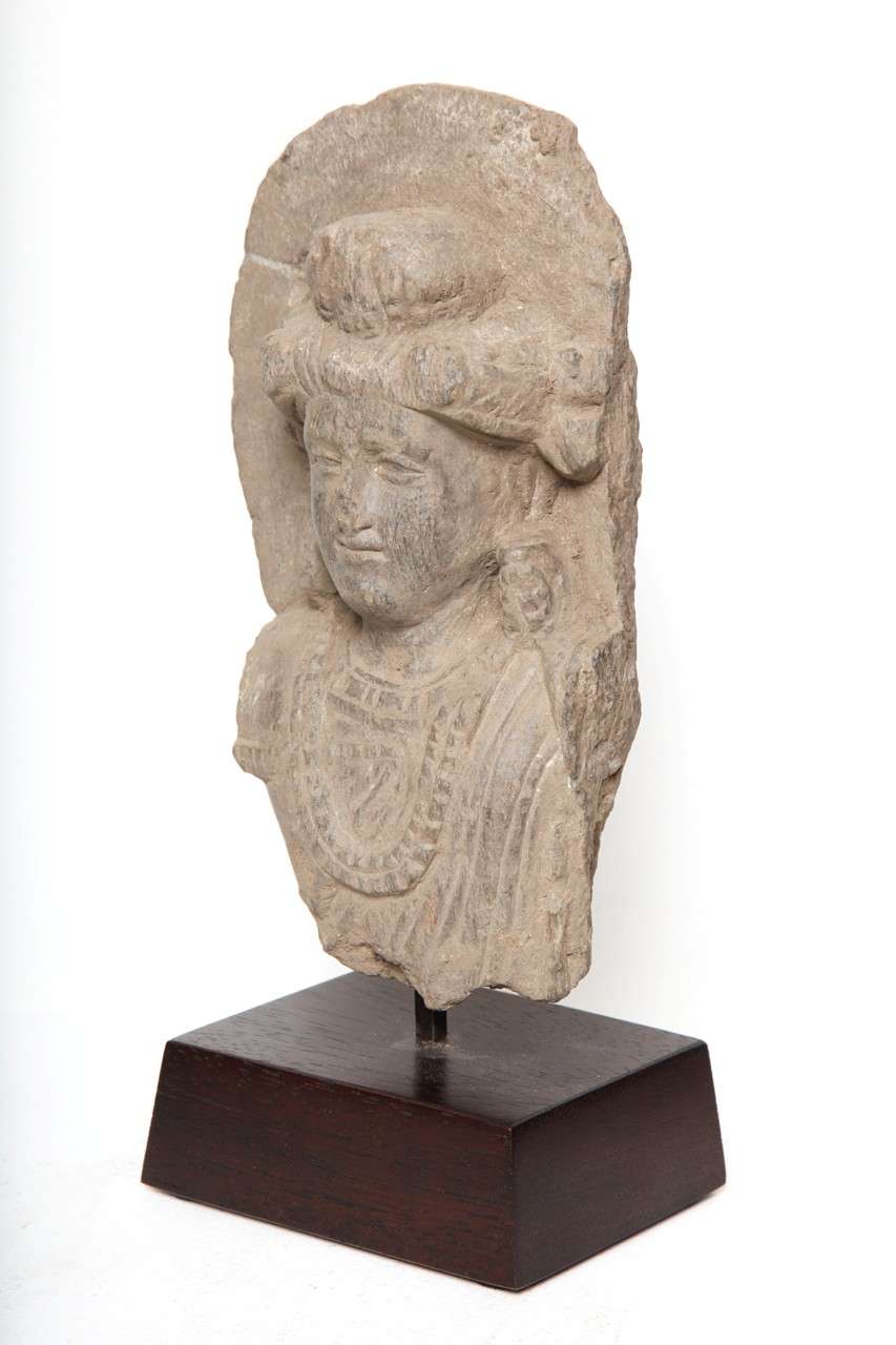 Carved  gray schist stone relief bust of the prince with textured hair arranged in an usnisa bun upon his head, and he is adorned with earclips and strands of bead as well.  

7 inches + custom mount which adds additional height.

Ex W.