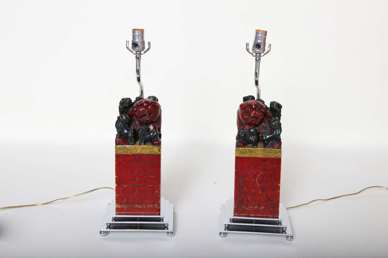 Pair of red, black, and gold carved wood foo dog lamps with Chinese script on a chrome base.
