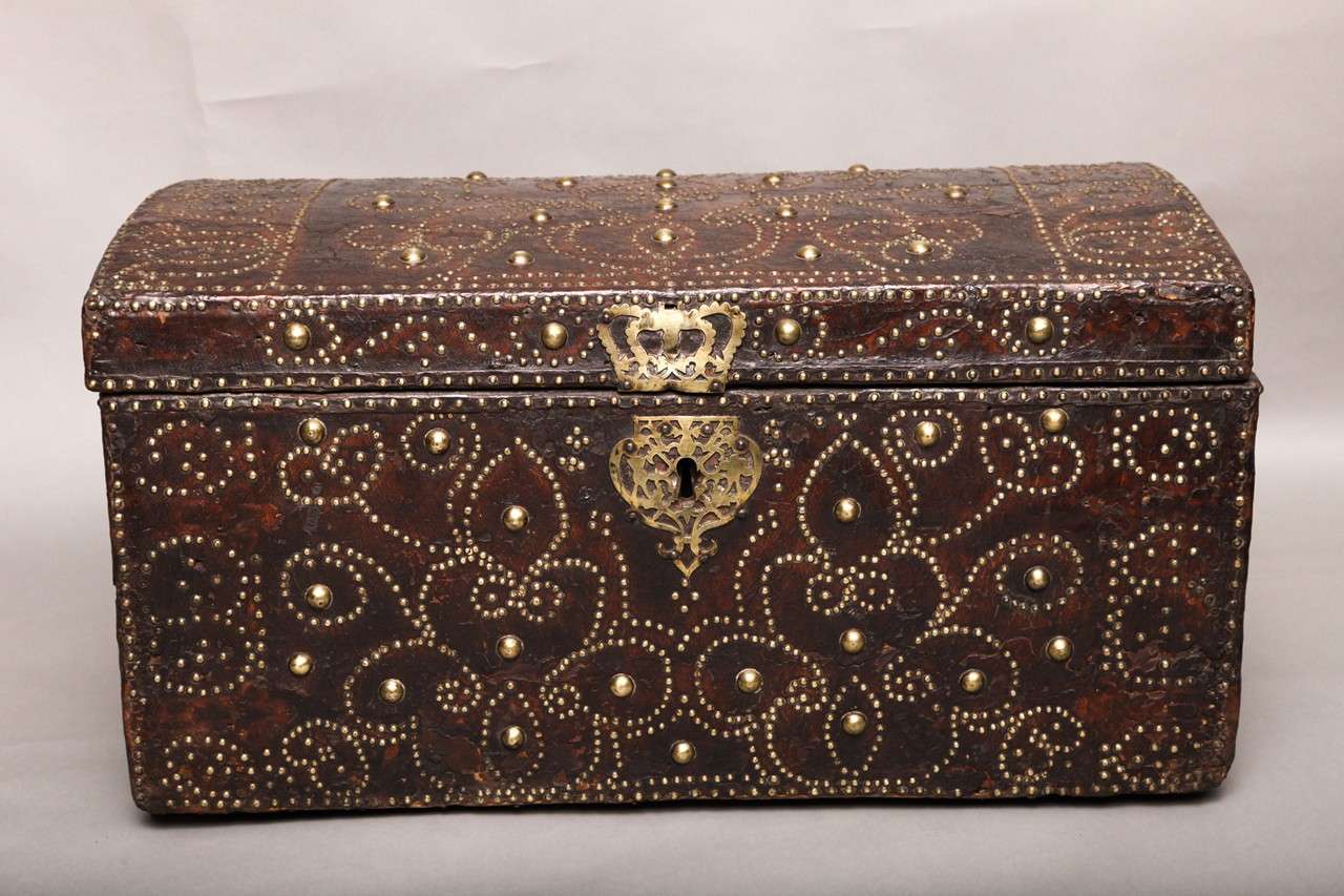 Very fine early 18th Century leather travel trunk in beautifully brass and iron studded Spanish leather, having tulip and clover design, original coronet and heart escutcheons and wrought iron hinges and handles, the whole with beautiful patination,