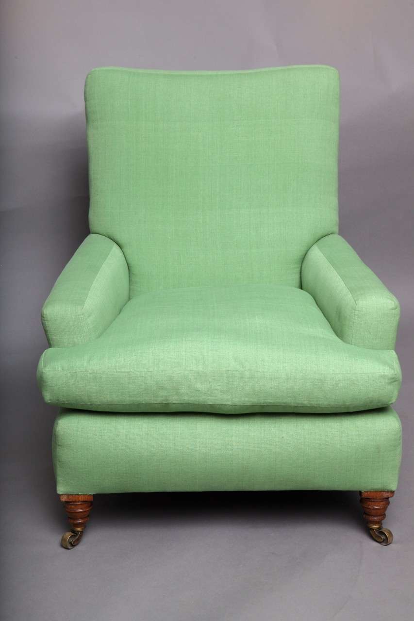 19th Century English upholstered club chair, the square back over square arms, standing on original turned legs and brass castors, in the manner of Howard and Sons.