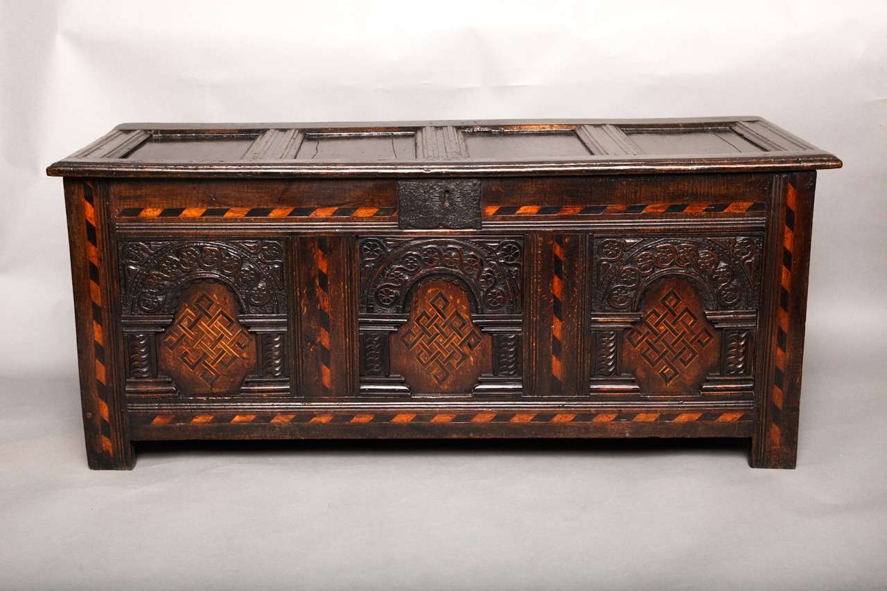 Very fine early 17th Century English oak coffer, the four panel lid having molded stiles, over arcaded paneled, front, the rails and stiles inlaid in diagonal banded stringing in bog oak and holly, the three panels inlaid in geometric knots with
