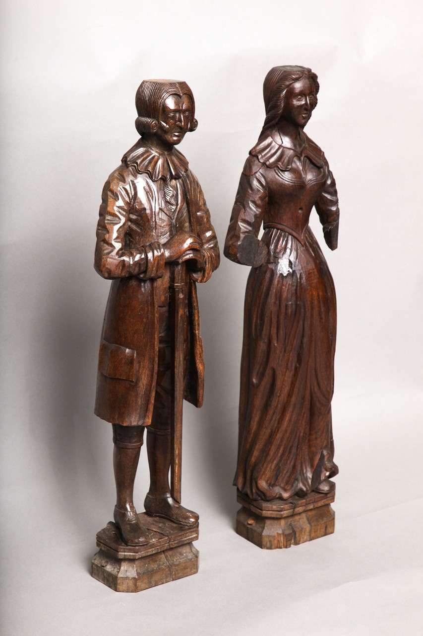 Rara coppia di figure intagliate in legno di quercia raffiguranti probabilmente Sir Robert e Lady Brown, 1735 circa. Lui è raffigurato con un taglio di capelli da paggio, con un colletto di pizzo e con un bastone in mano, lei con un gilet in vita su