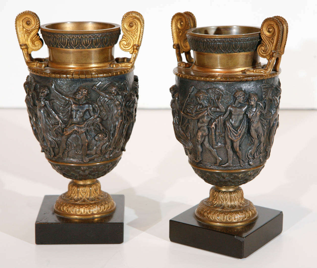 Pair of petite, hand-cast, silver and gilt bronze urns with neoclassical reliefs on granite bases.