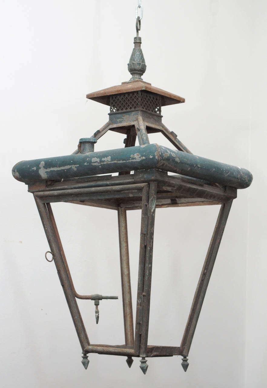 A large, painted iron lantern, having a fuel reservoir incorporated in its frame, and an intricate top with a pine cone finial over a lattice form chimney.