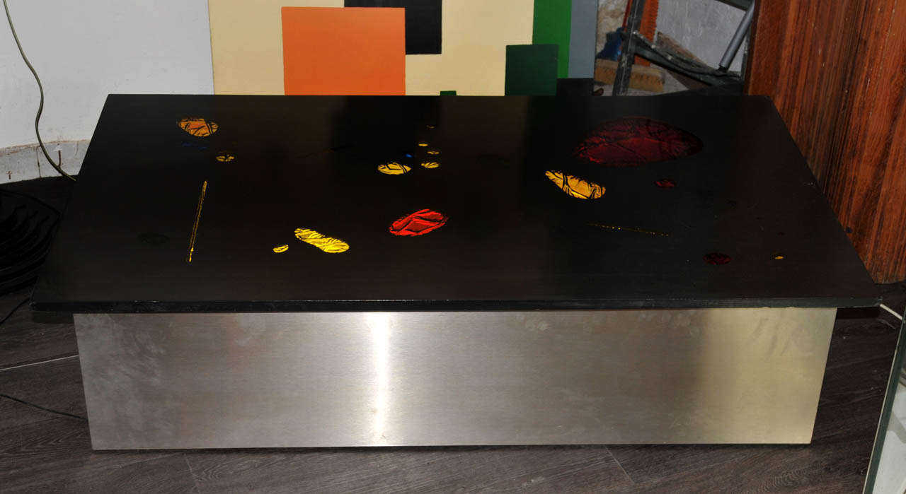 1980's coffee table. Slate top with colored glass inlays and two inside neons lights. Brushed steel base. One switcher on the side. Wired for European use. Good condition. Two small impacts on the slate top. Normal wear consistent with age and use.