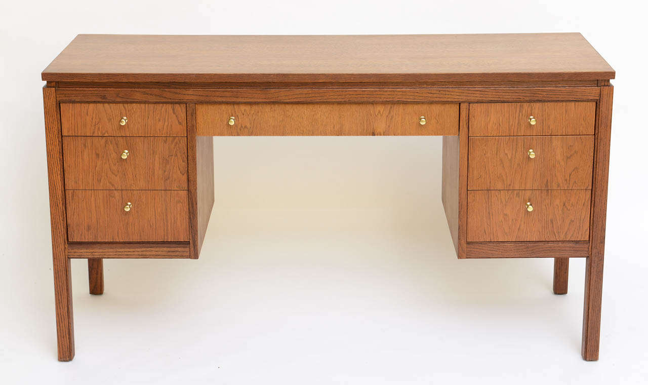 SOLD  Elegant small scale executive desk finished all around in beautiful combed oak with brass pulls in the style of Edward Wormley.  Featuring a centered pencil drawer, a bank of three drawers to the right, and two to the left (designed to look