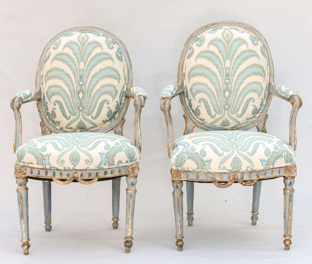 Pair of Fauteuils, each having a painted and parcel gilt finish with natural wear, having oval backs, continuing to padded arms, raised on downswept terminals, crown seat on bowed fluted rail, raised on round fluted tapering legs, ending on touipe