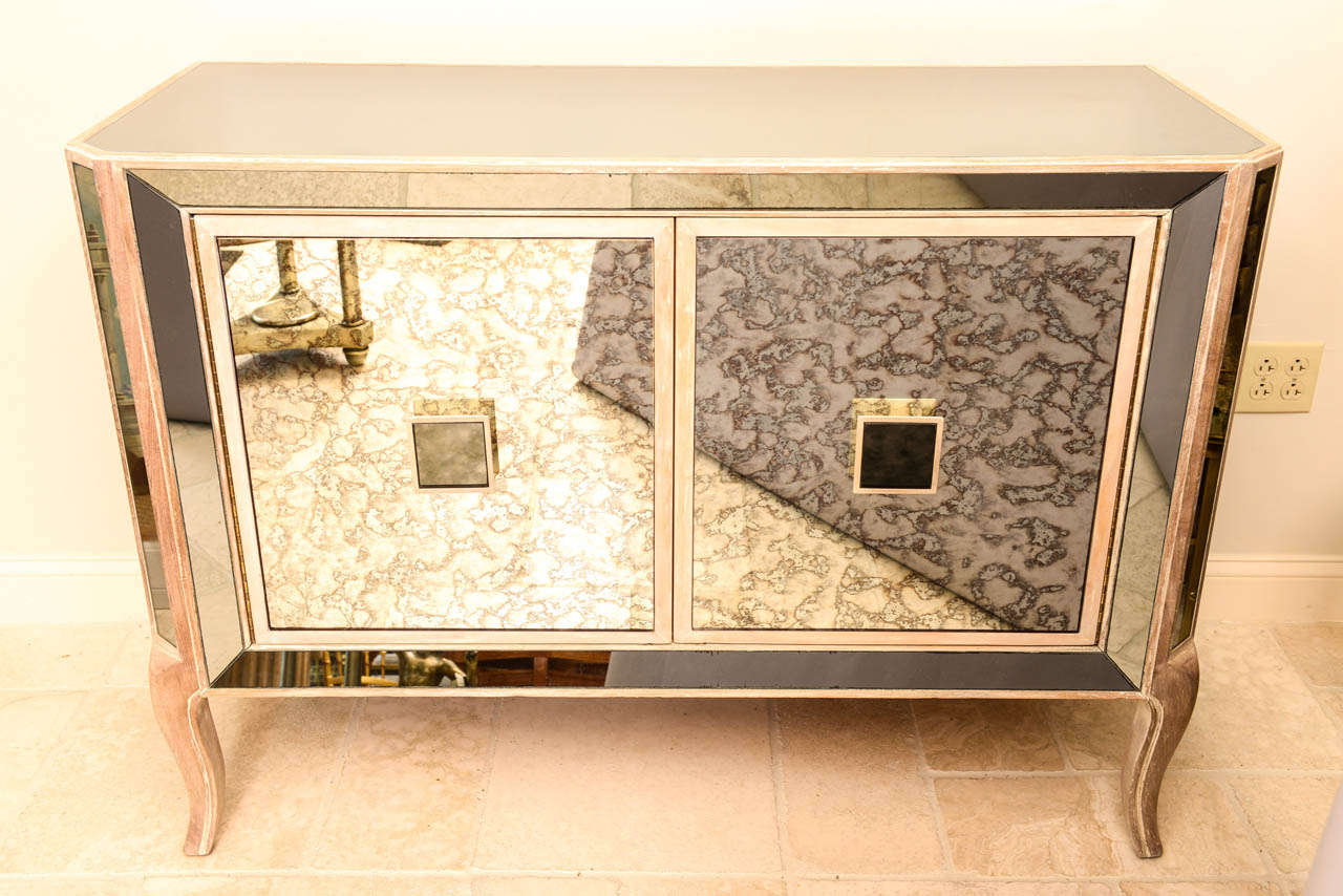Cabinet, having all surfaces covered in mirror, two cabinet doors with spotted mirror and square mirrored pulls; doors open to three drawers on right and shelf on left, raised on stylized cabriole legs of pickled wood.