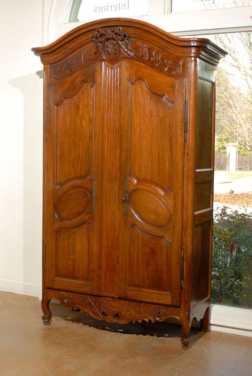 A French period Louis XV walnut armoire with bonnet shaped pediment, ribbon-tied medallion and carved skirt from the mid 18th century. Born in the middle of the reign of King Louis XV, this French armoire features a bonnet shaped pediment,
