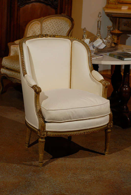 A French Louis XVI style barrel back painted and gilt wood bergère chair from the 19th century with new upholstery. This French bergère features a barrel back, adorned with twisted ribbons on the upper rail, flanking a central Louis XVI knot carved