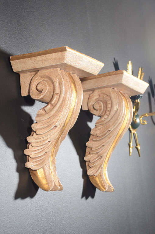 Hollywood Regency wall brackets with classical acanthus leaf design. Hand-carved with crackle pattern Gesso finish and gilt details. Made of plaster coated wood and have a top shelf with fluted and scrolled design. 