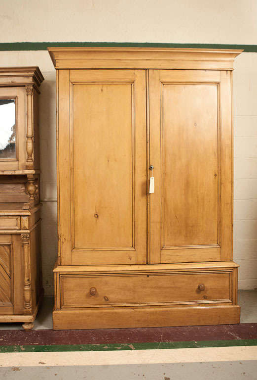 A very fine English pine armoire of exceptional understated elegance.  Built in three pieces it features a deep base with single delicately hand-cut dovetailed drawer, a two door centre section with wide swinging flat-panelled doors opening to