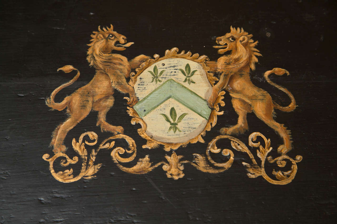 A 19th century English storage chest hand-painted with a decorative lion crest sits on a custom-made solid wood stand.