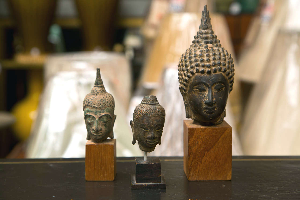 A grouping of three small Bronze Buddha heads mounted on wood.