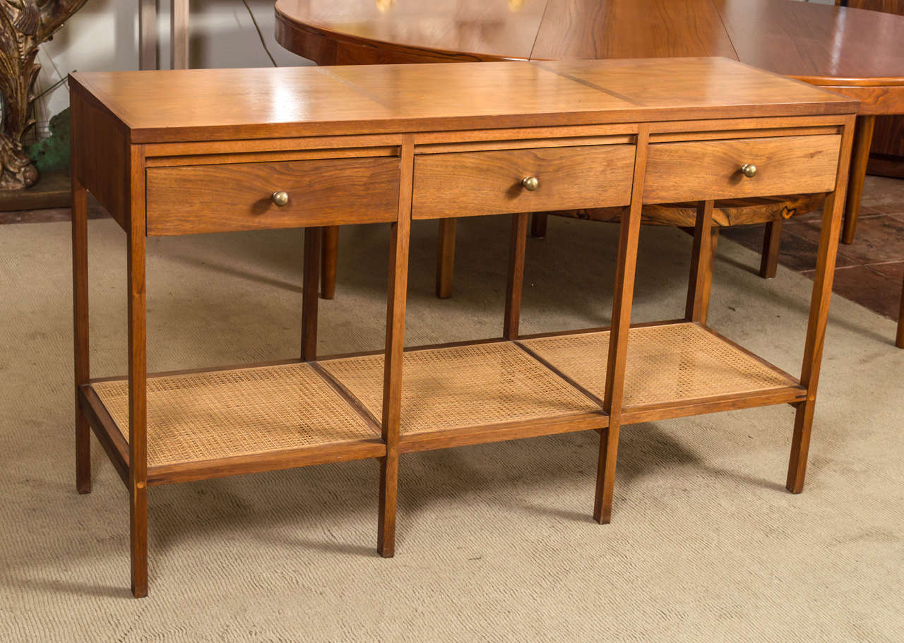 A Paul McCobb design for Lane, from his Delineator line. This is the rare Console table, is Walnut with Rosewood, three drawers and below them is a cane shelf. Very nice construction, great details. Knobs are not original.