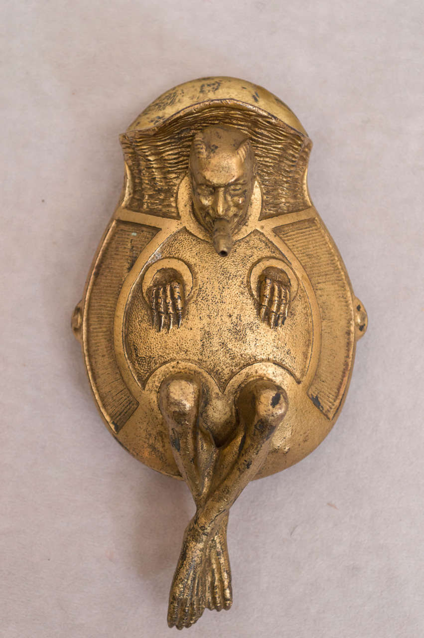 This highly whimsical wall mount devil/match holder and gas lighter is a rare item indeed. There is a pocket behind the devil to hold matches and the side of the devil is the match strike. There is a hole in the cigar which leads to a back opening
