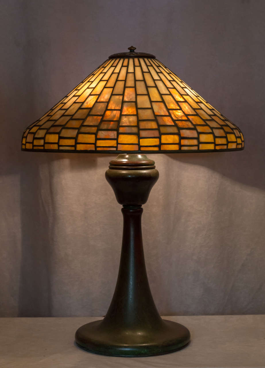 This simple and elegant lamp was by the designed and manufactured by the greatest American lamp maker, Louis Comfort Tiffany. The base and shade are both properly signed and in amazing condition. The shade barely has a heat line, and the bronze base