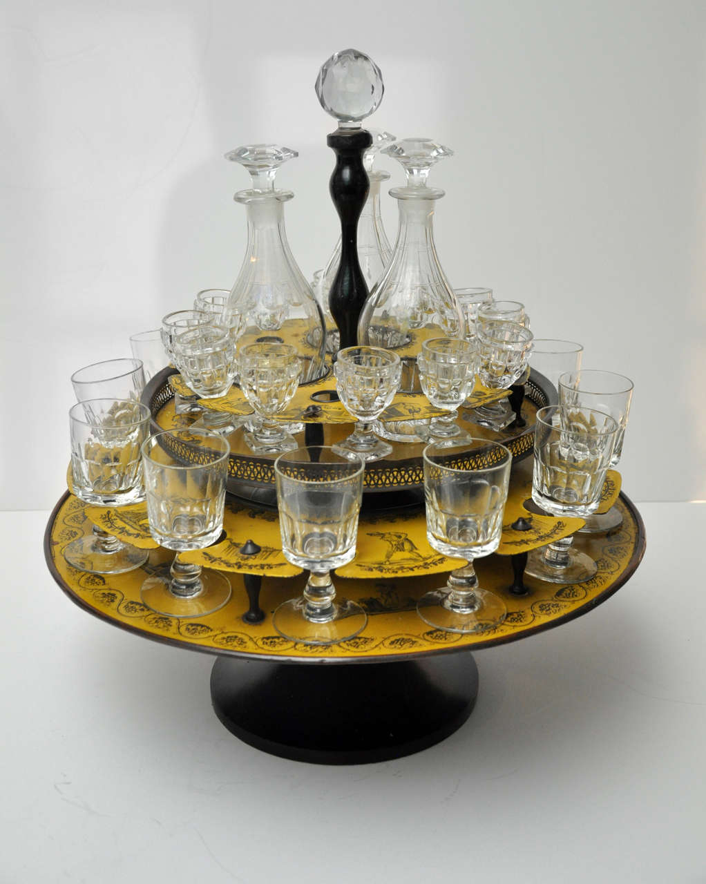 French Yellow Tole Peinte Two Tier Glassholder,
includes 12 small glasses, 12 large goblets, 3 decanters, 
Circa 1840