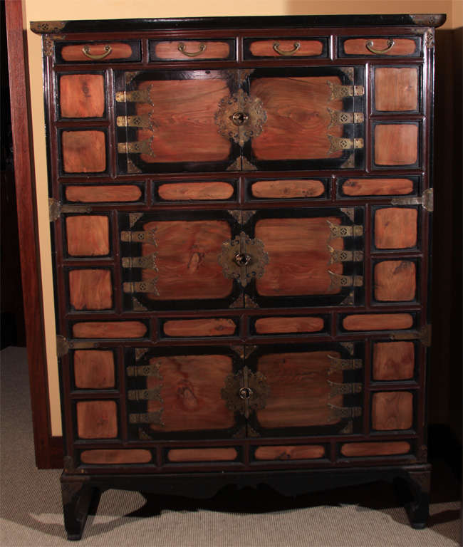 Tall Korean three tiered clothing chest (samch’ung jang).  The frame of the pine wood (so namu) chest with deep red-brown lacquer finish and floating panels, doors and drawers with wiped black lacquer finish. The fine brass fittings and hardware