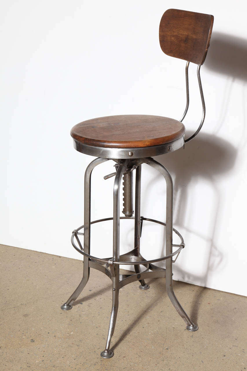 Comfortable early 20th century adjustable riveted steel and hard wood toledo stool with adjustable wood back support. Adjustable height range; seat measures 27.5