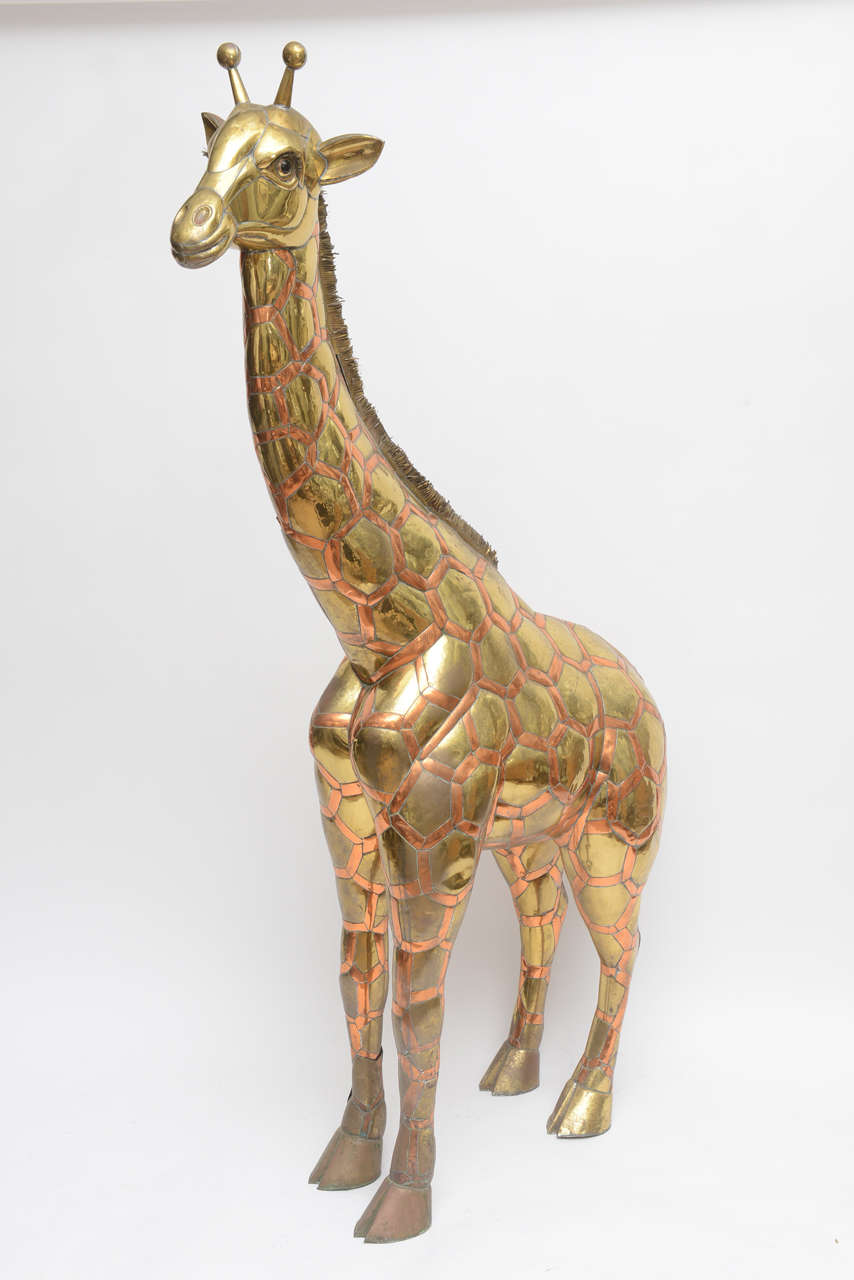 Large, 6ft tall giraffe by Sergio Bustamante. Standing, brass and copper forged giraffe. Glass inserted eyes. Sheered strips of brass and copper make up the tail, while antenna top of this beautiful piece of handmade artwork.