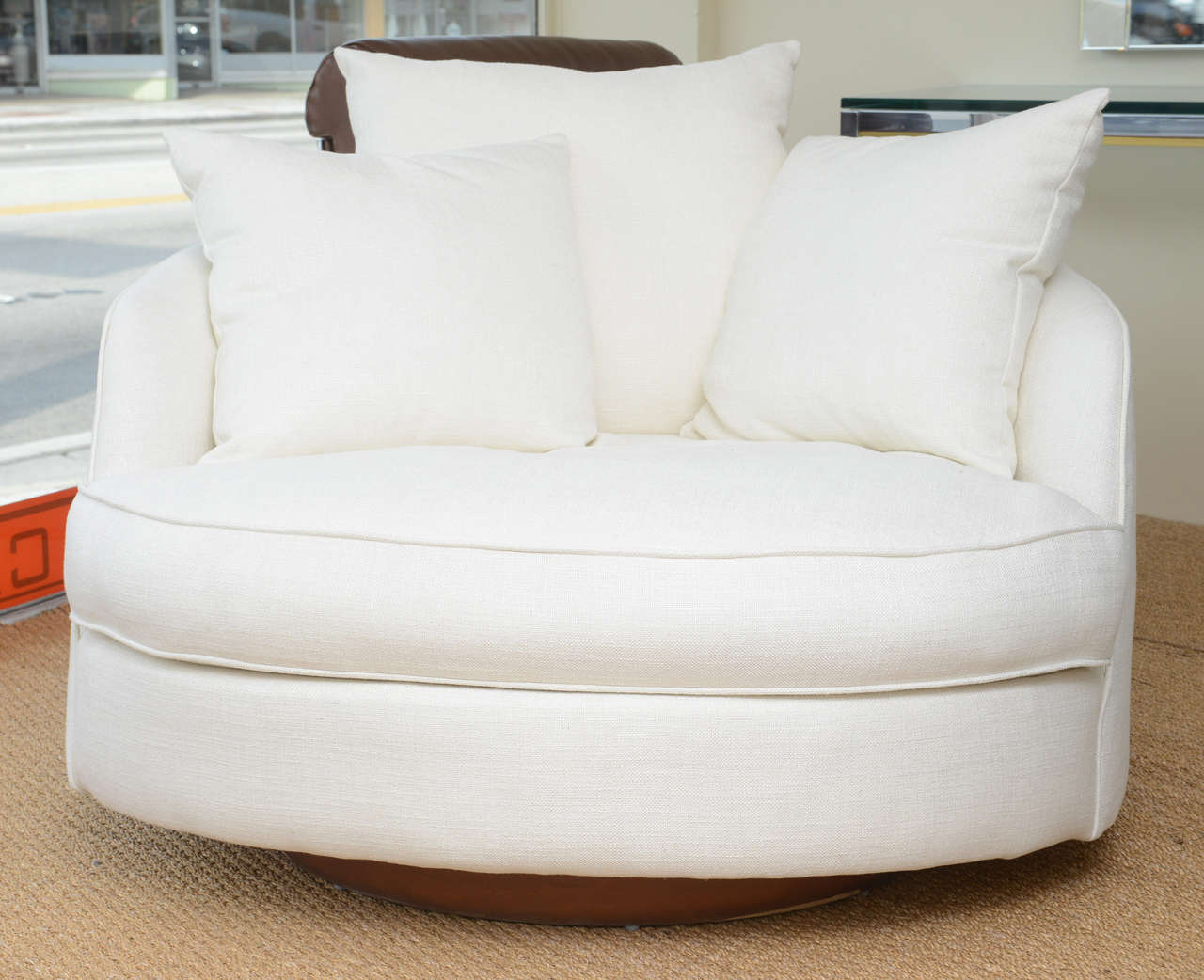 Milo Baughman MOD-style swivel round lounge chair on a wood platform round base. Newly upholstered in an off white linen textile with three lumbar pillows, also in the same textile. Two standard size, and a back pillow, larger for back support.