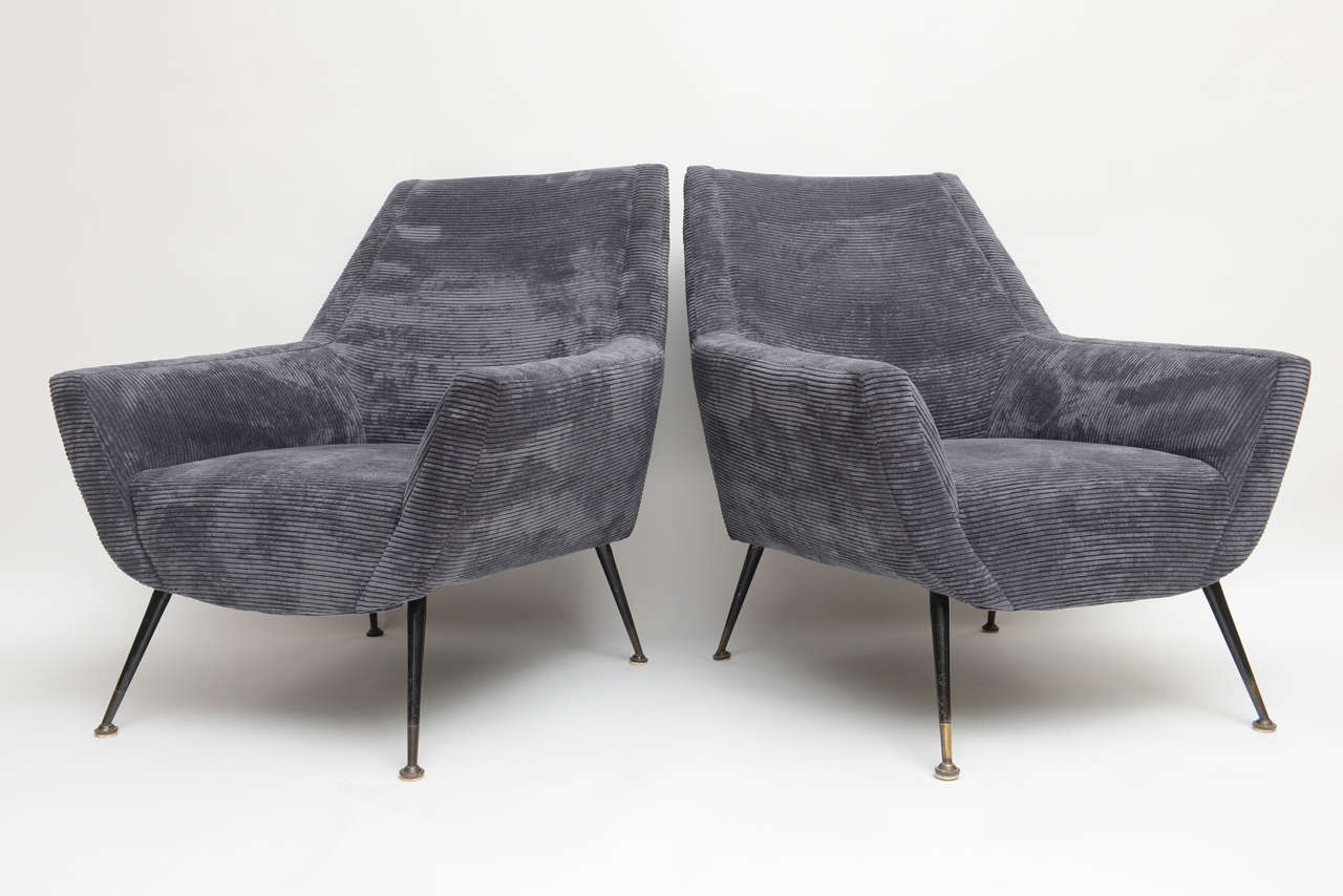 Pair of 1950s, Italian lounge chairs with slanted metal legs and brass capped sabots. Newly re-upholstered in a midnight ice blue corduroy textile, with handsome stitching to inset sides, contoured to the shape of the chair.
Low seating, square cut