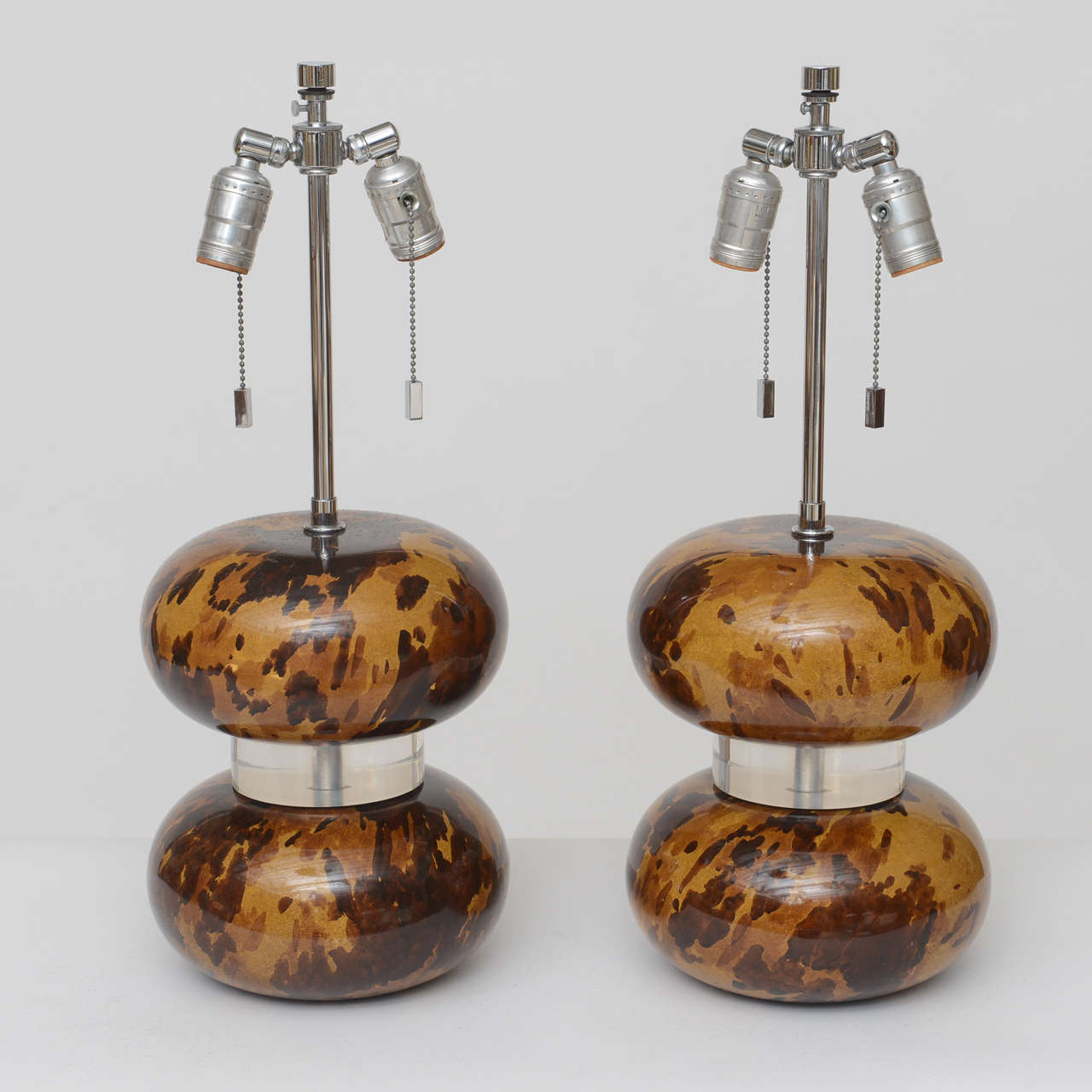 Gorgeous pair of Karl Springer table lamps, circa 1980. Distended orbs with faux tortoise shell finish are separated by a thick Lucite disk. All original chromed hardware. Adjustable harp starts at 22