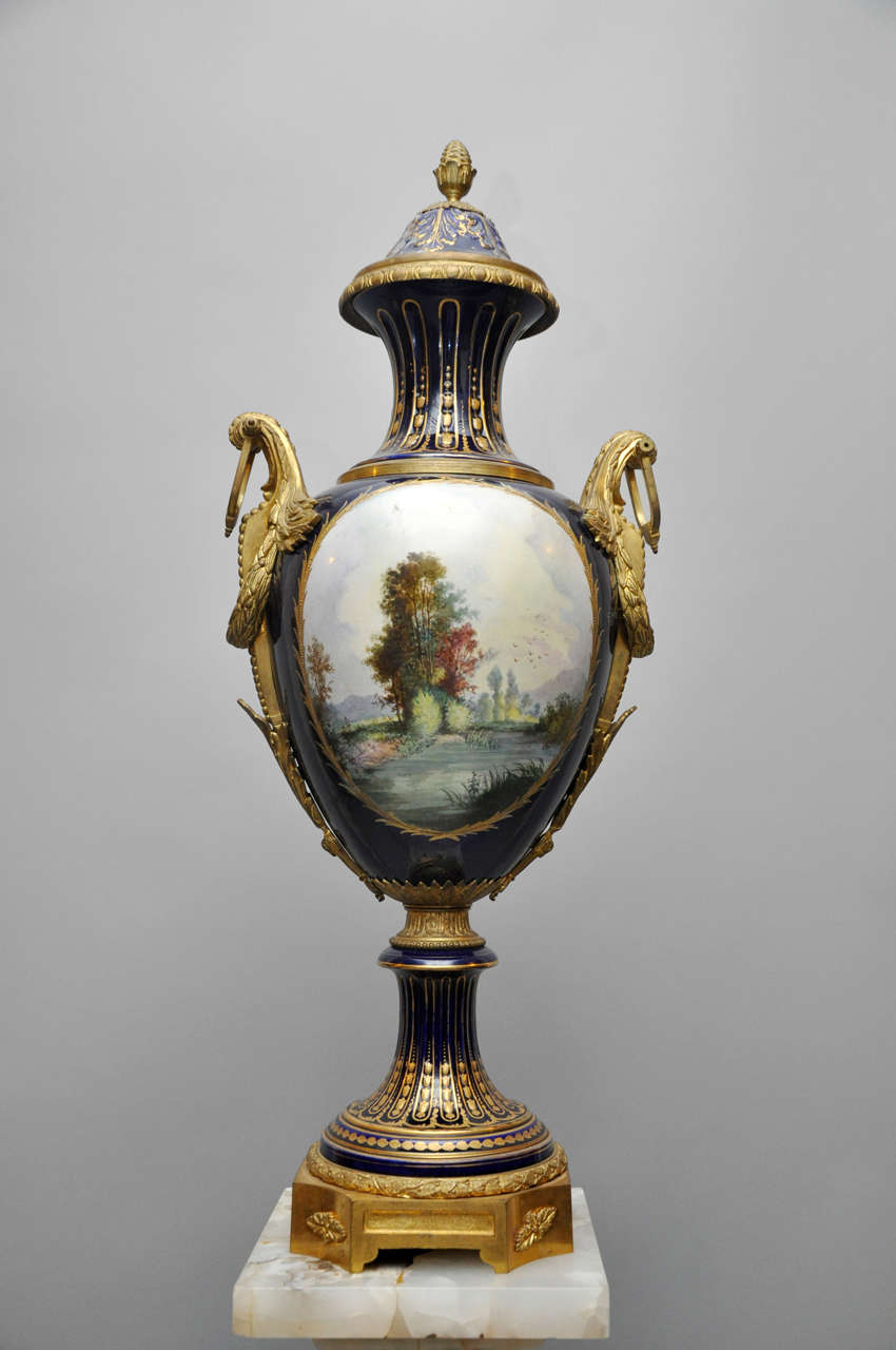 Monumental Cobalt Blue Gilt Bronze Sèvres urn. Cobalt-blue baluster form with tooled gilt bordering cartouche centered with polychromed enamel romantic painting depicting a man serenading with his mandolin to two maidens, titled 