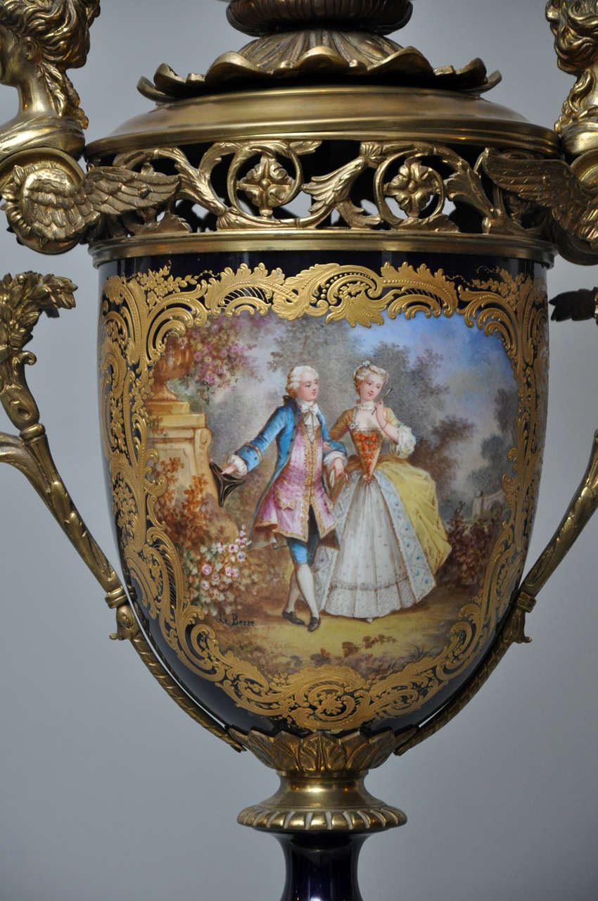 Palatial Sèvres style vase supporting a six light bronze candelabra, converted to electric. Cobalt blue-ground baluster form vase, cartouche outlined with chased gilt surround depicting a painting of a courting scene between a man and maiden, on the