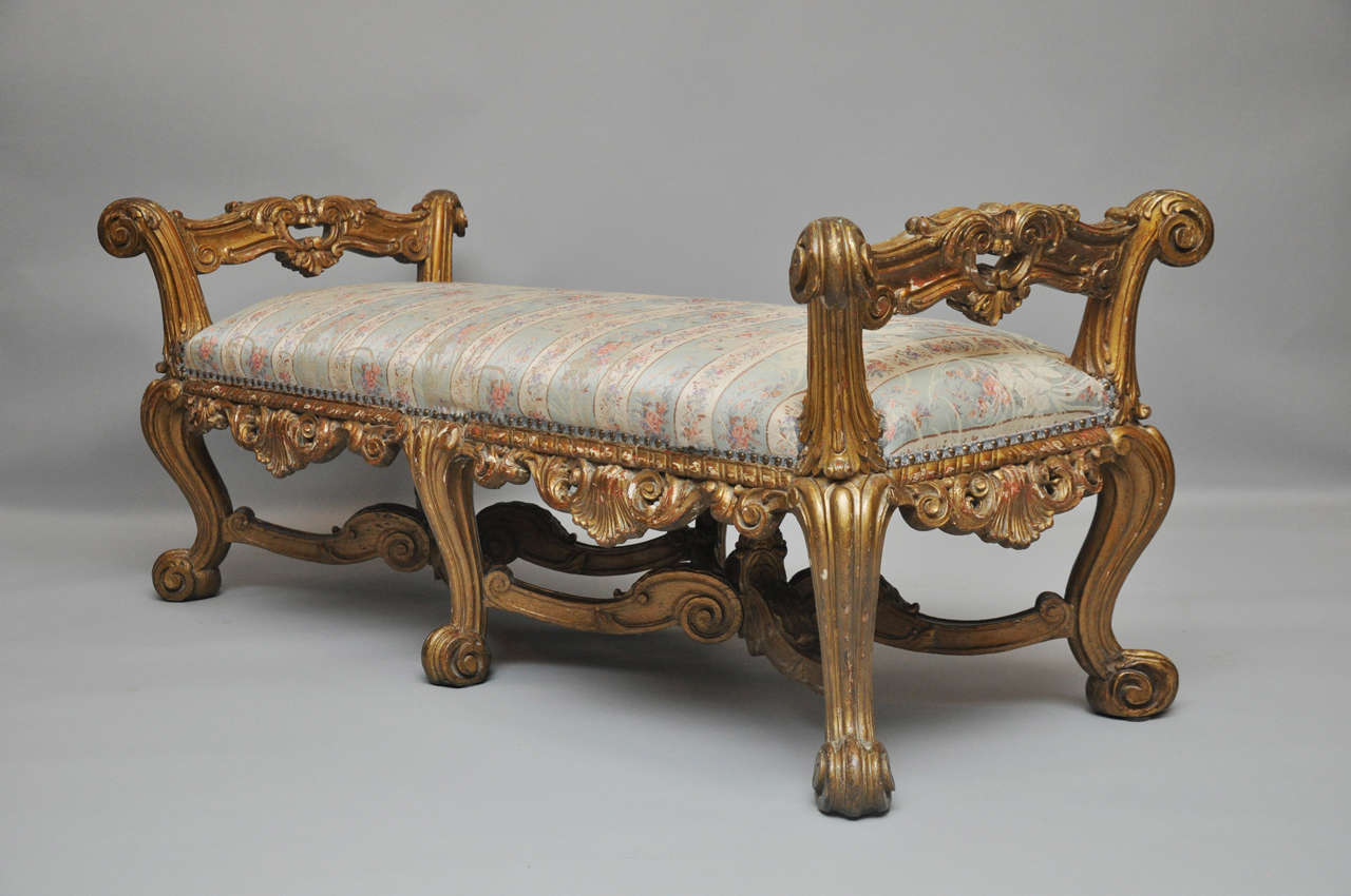 19th century French Rocco style gilt wood bench, with four sided elaborately carved apron, stretcher, and cabriole legs ending in scrolled feet.