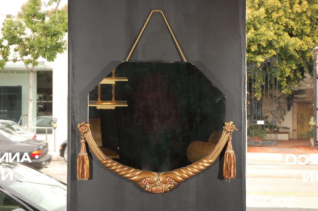 Miroir suspendu sculpté à la main avec glands d'origine assortis, attribué à Maurice Jallot. Le miroir a une forme octogonale et le haut s'arrondit en bas. Le cadre incurvé en feuilles d'or du bas présente des sculptures tournantes en couleur or et